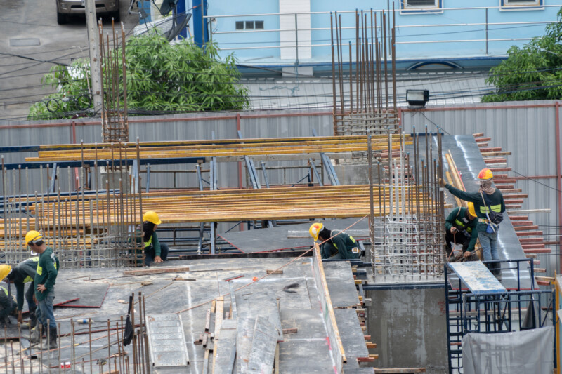 Aerial view of busy industrial construction site workers with cranes working. Top view of development high rise architecture building at noon.